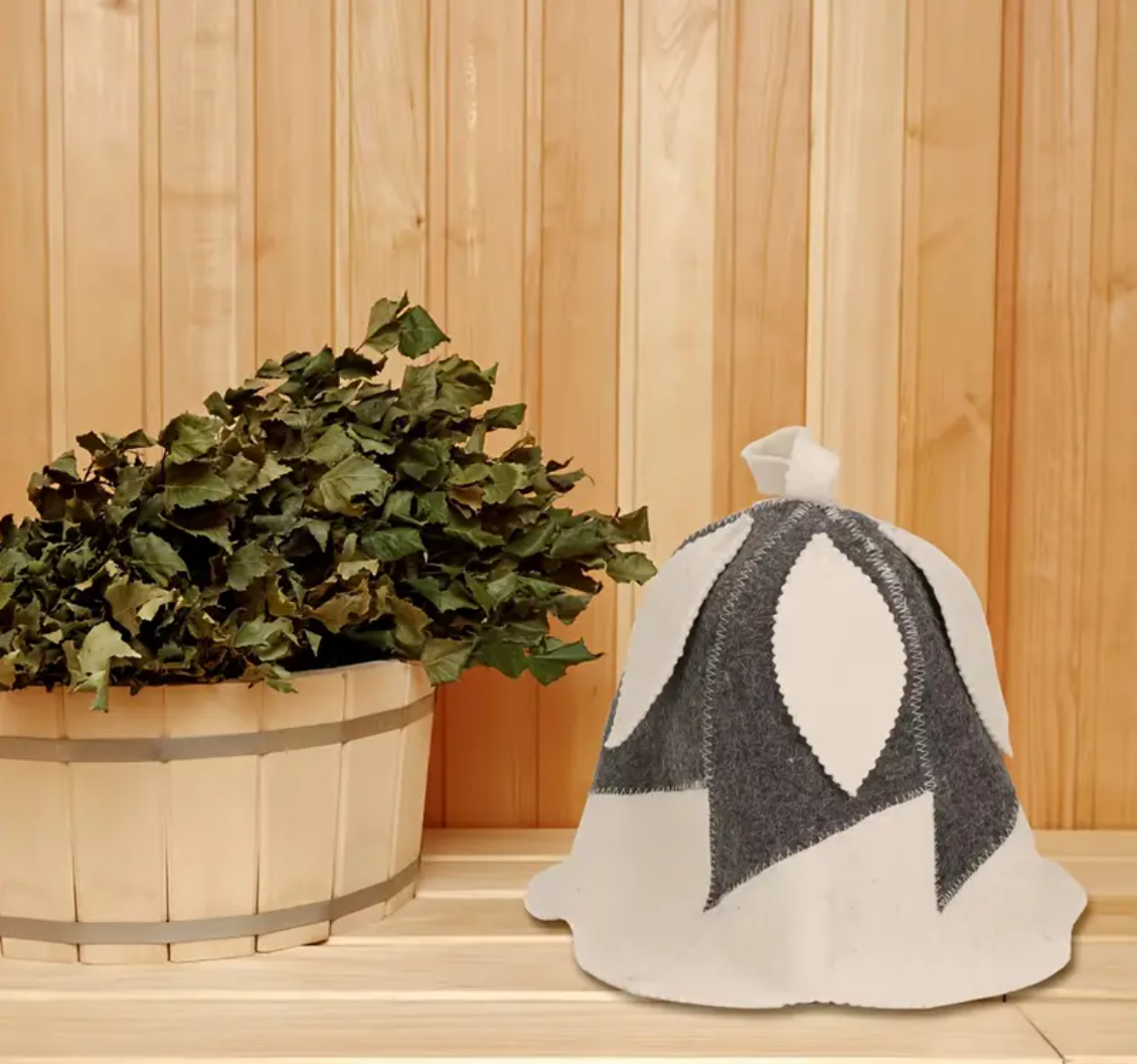 Wool sauna hat resting on a cedar sauna bench beside a birch whisk